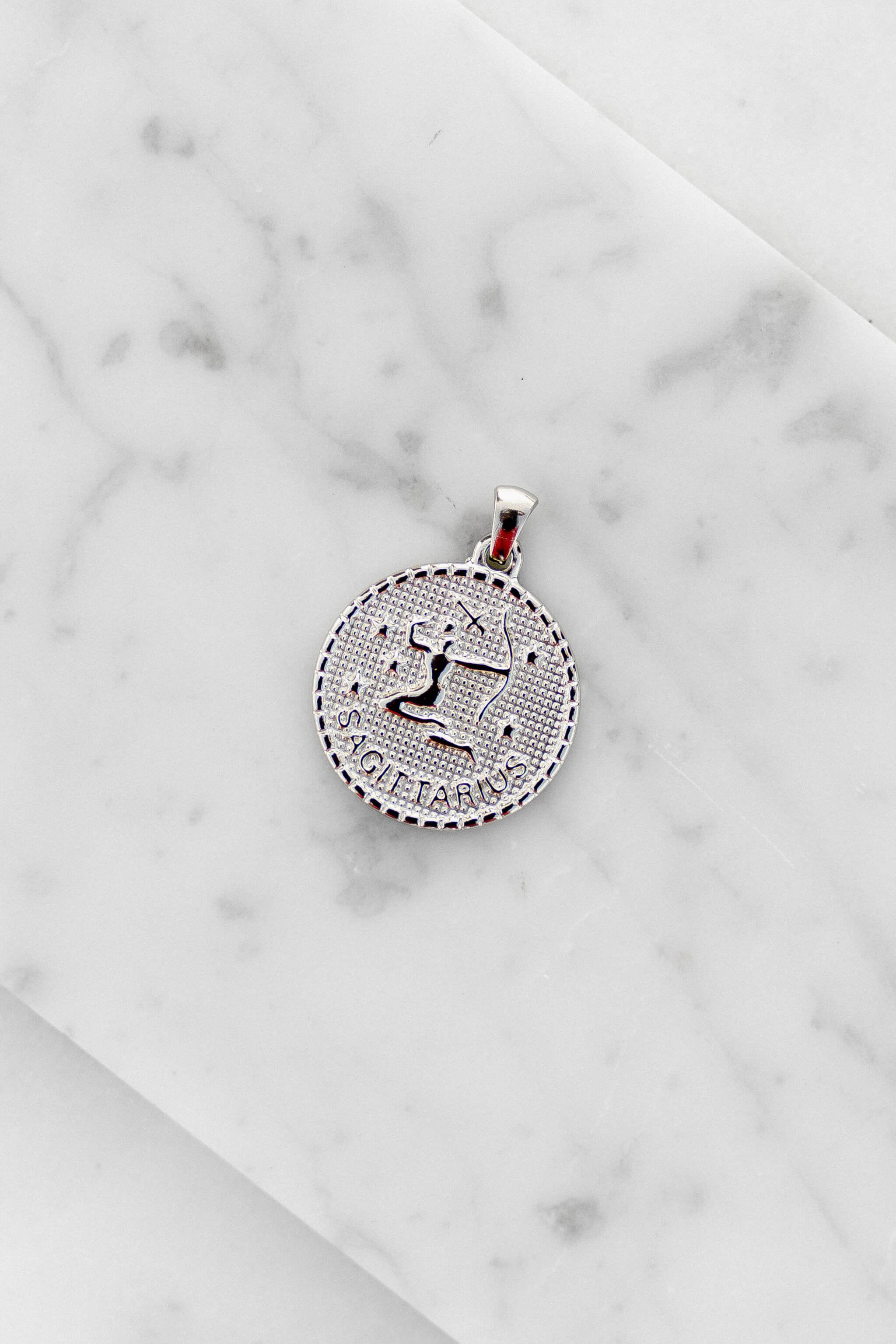 Sagittarius zodiac sign silver coin charm laying on a white marble