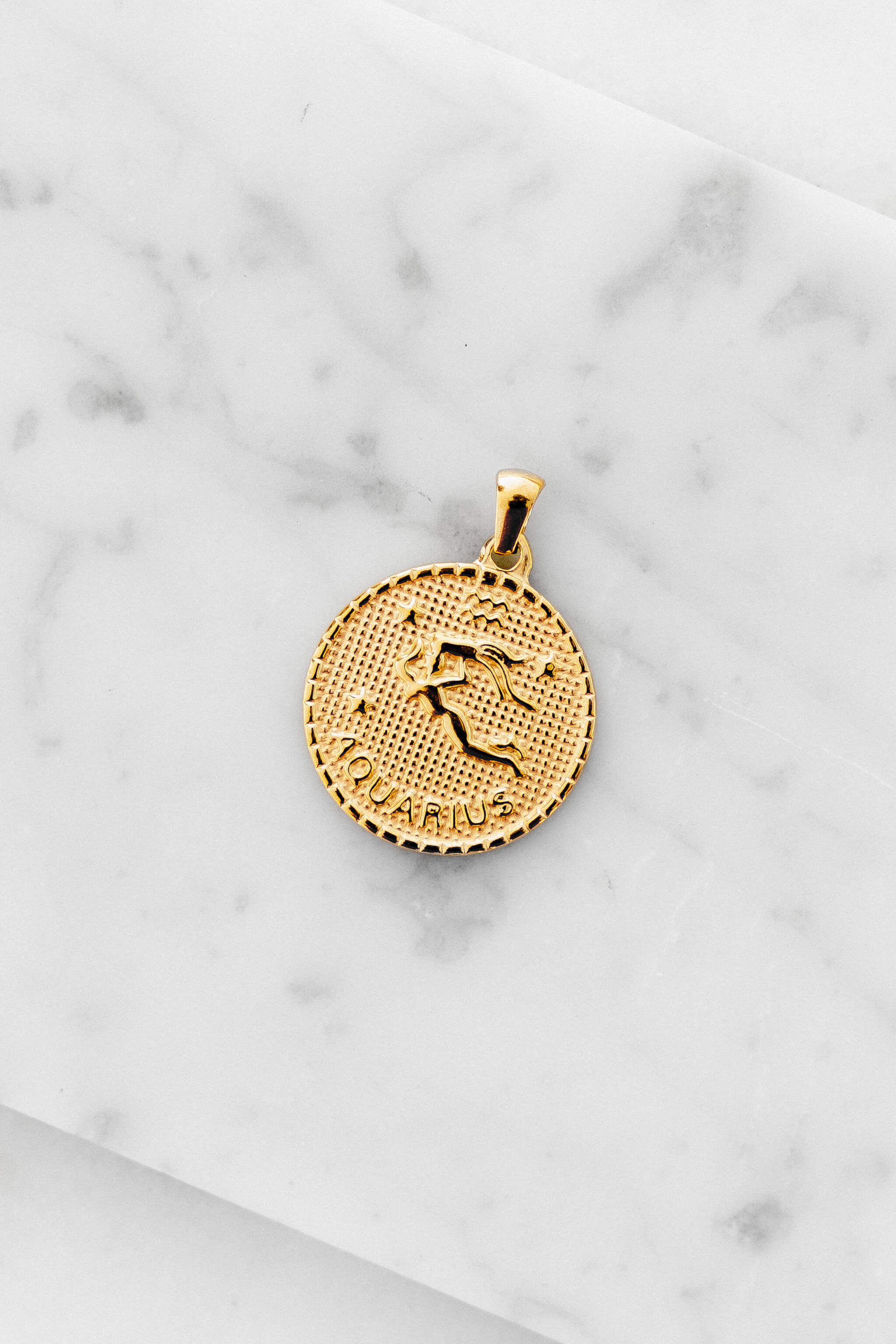 Aquarius zodiac sign gold coin charm laying on a white marble