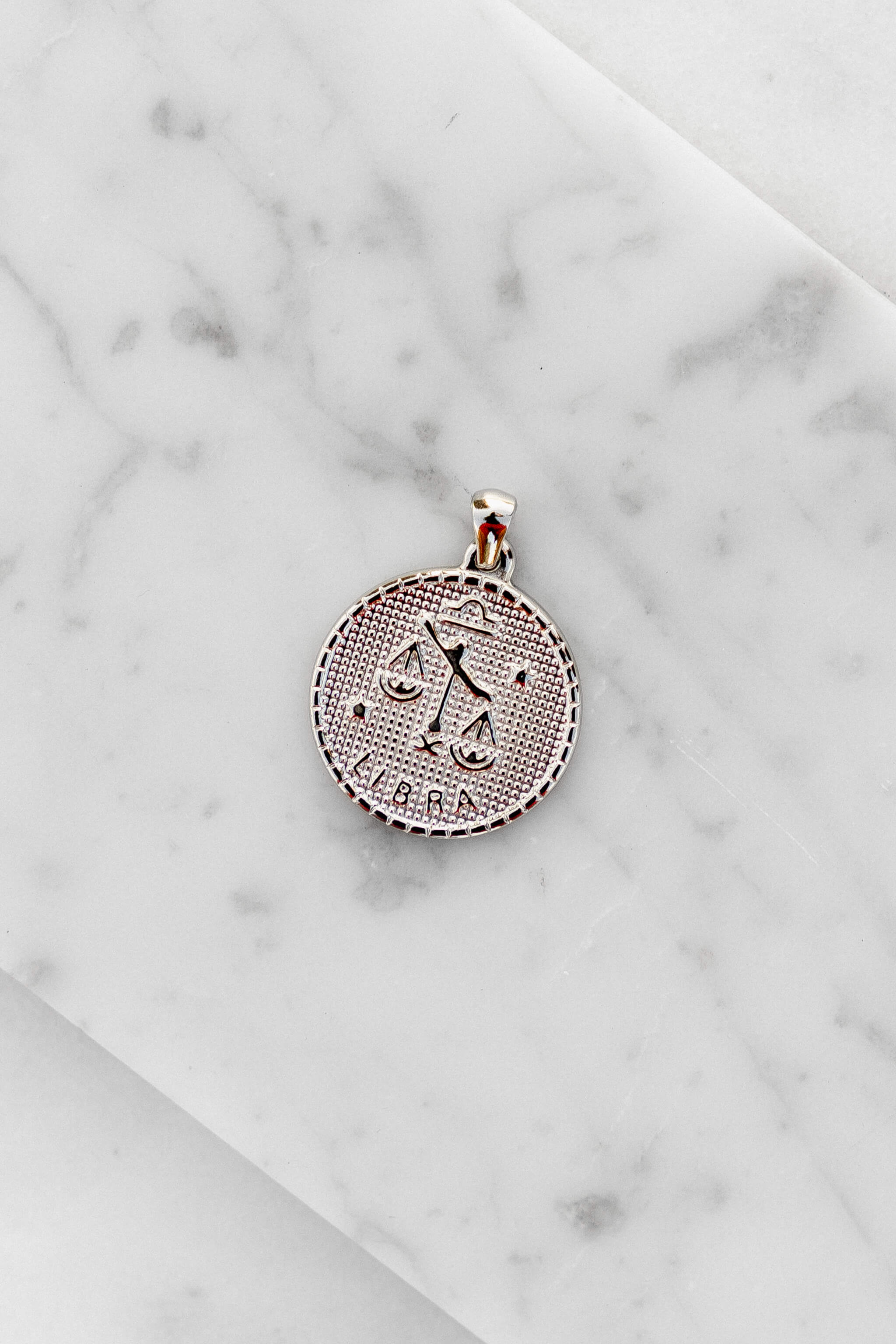 Libra zodiac sign silver coin charm laying on a white marble
