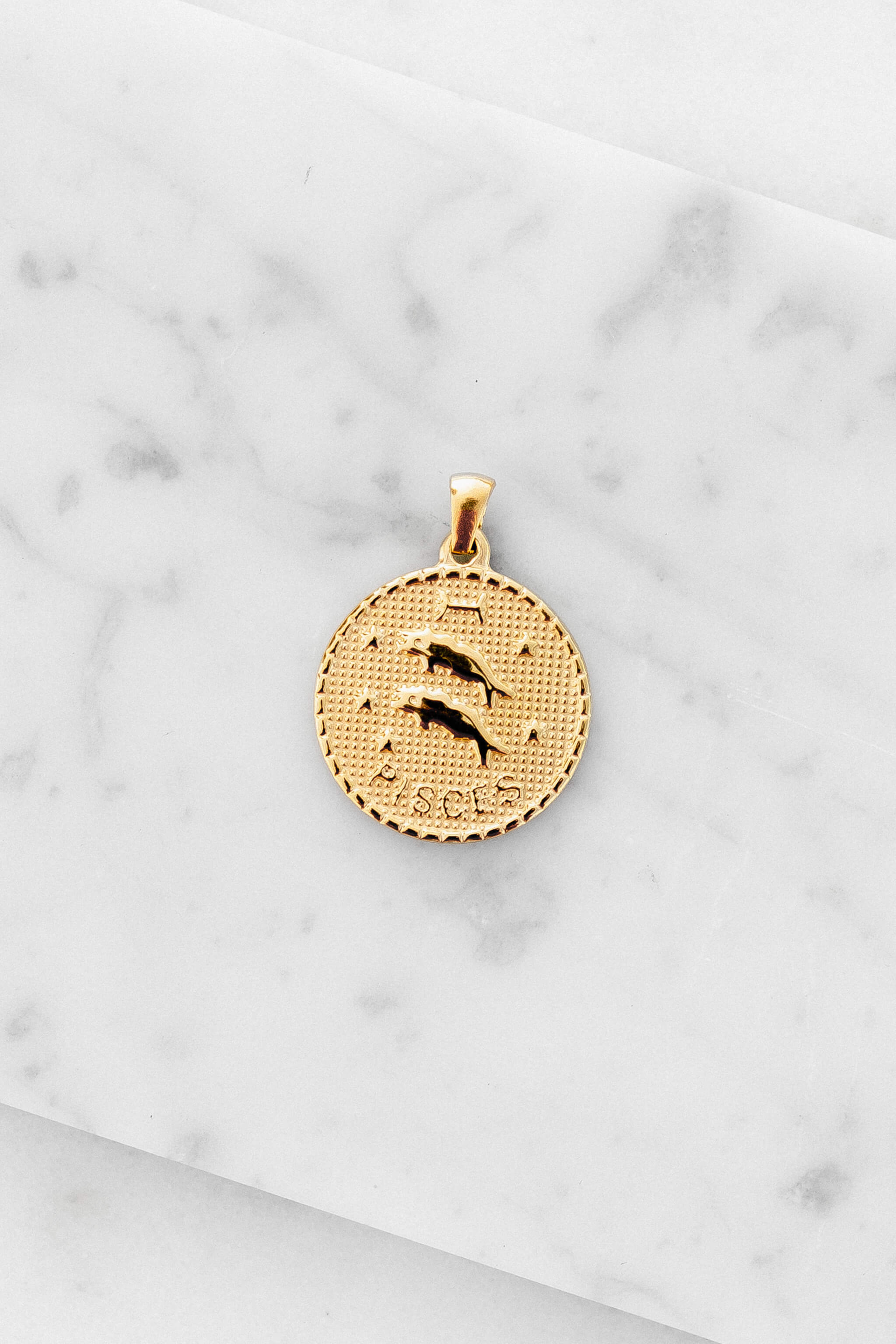 Pisces zodiac sign gold coin charm laying on a white marble