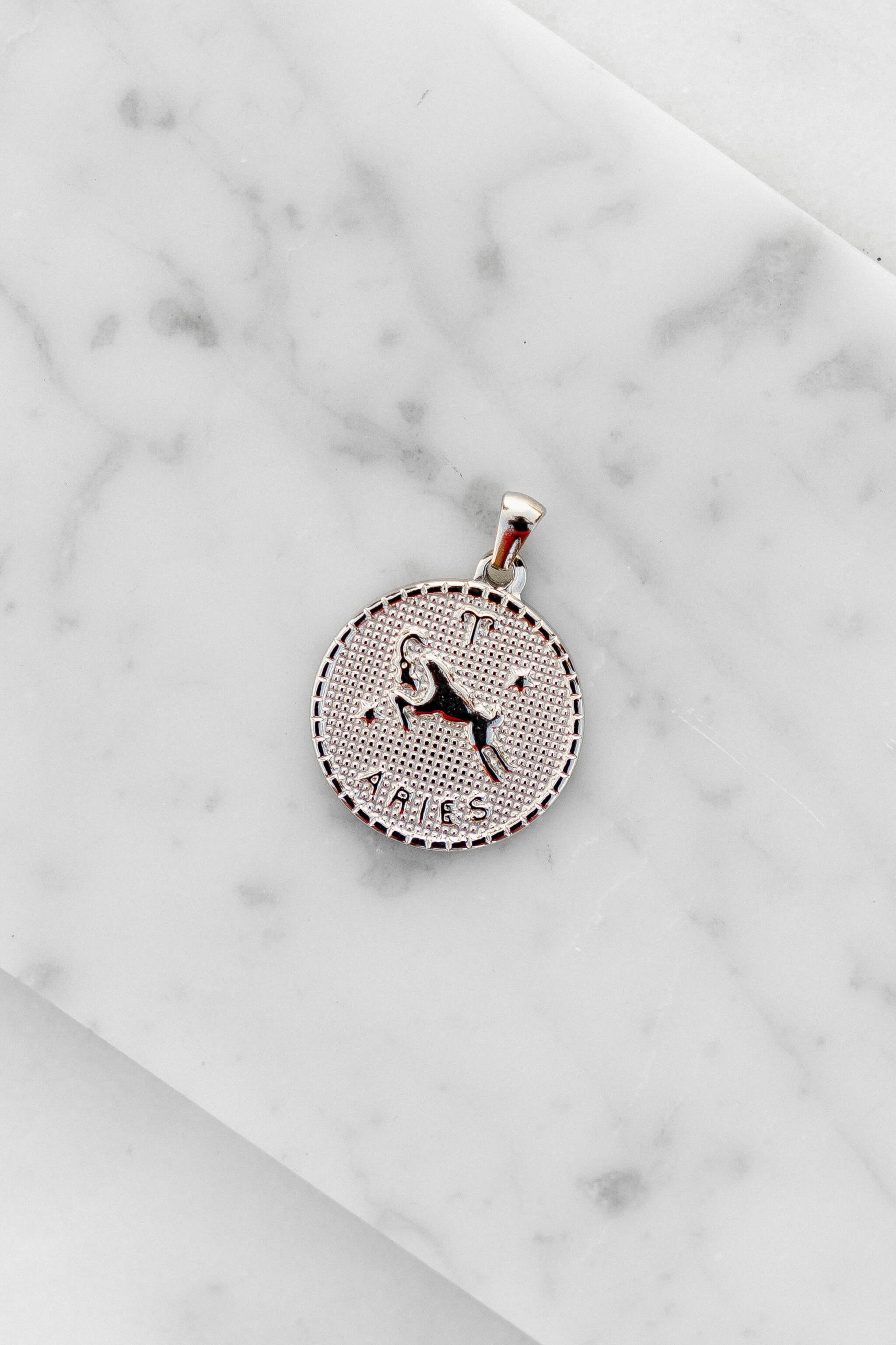 Aries zodiac sign silver coin charm laying on a white marble