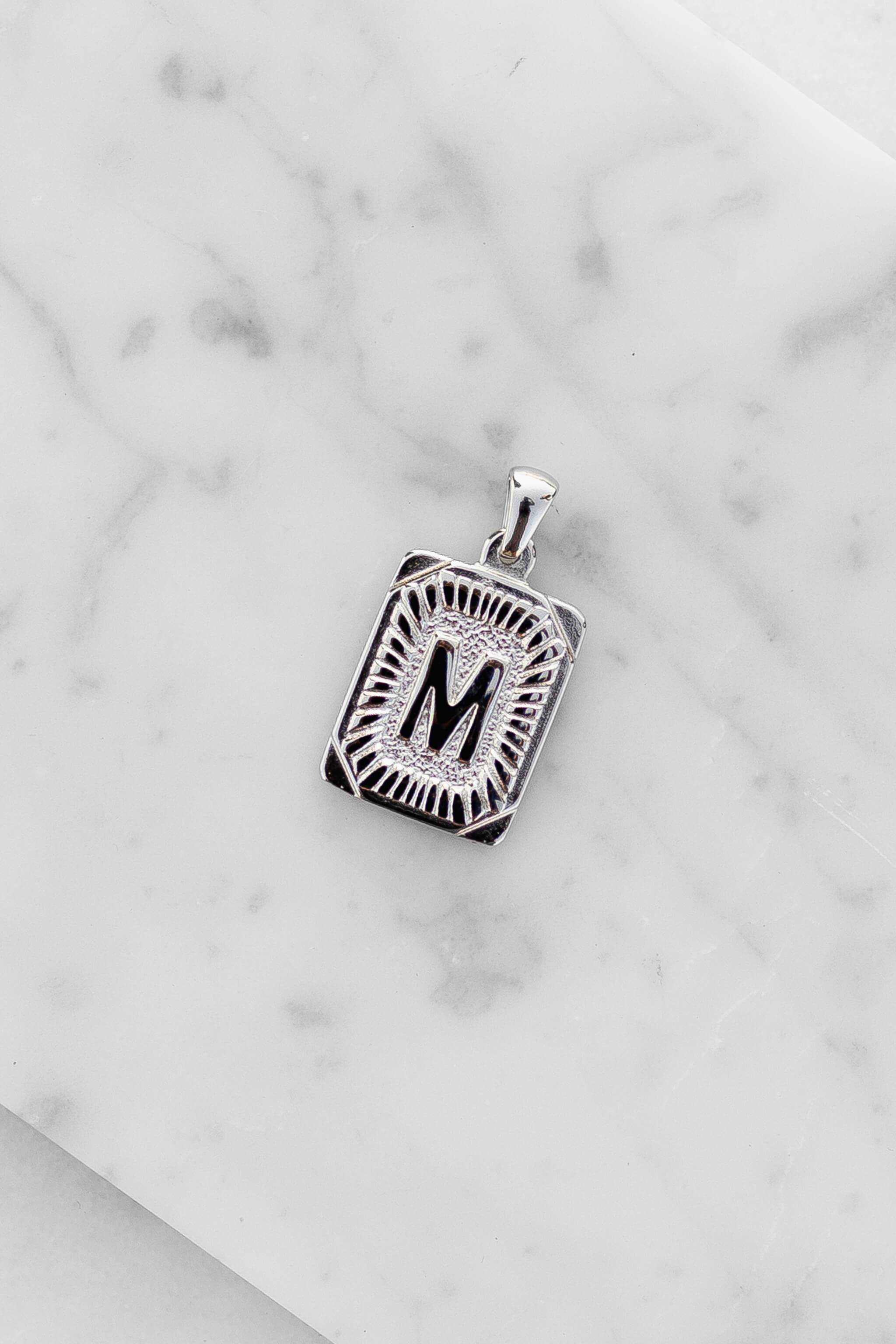 Silver Monogram Letter "M" Charm laying on a marble