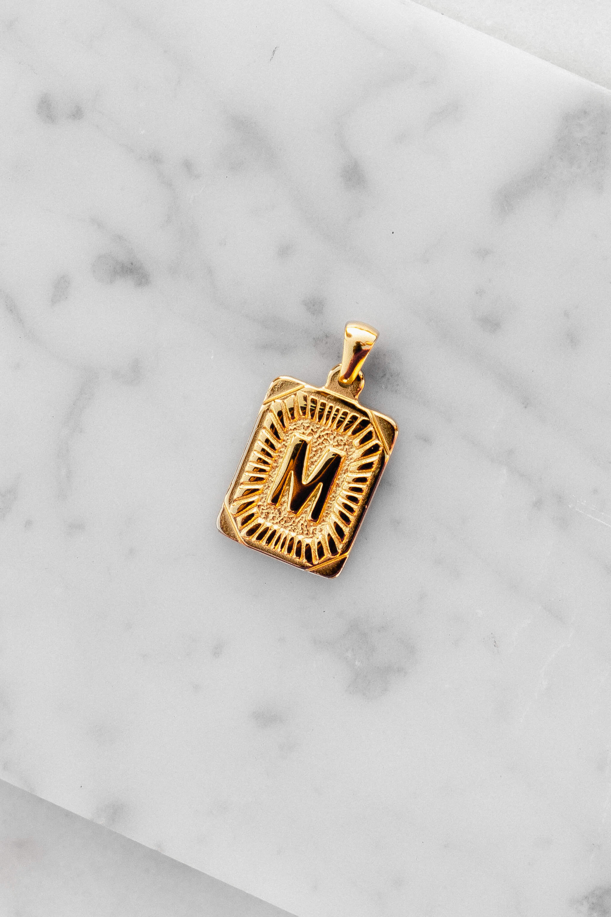 Gold Monogram Letter "M" Charm laying on a marble