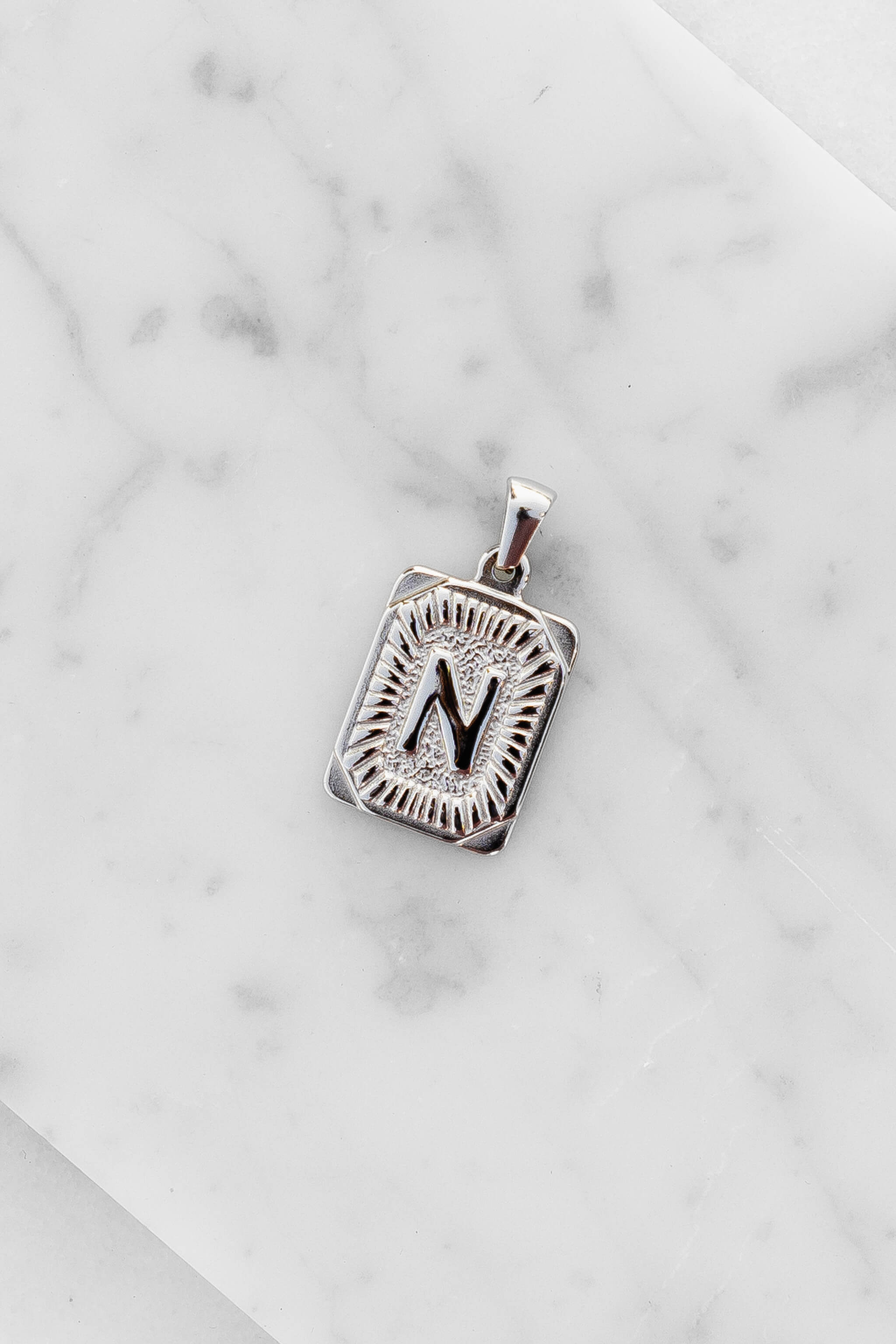 Silver Monogram Letter "N" Charm laying on a marble