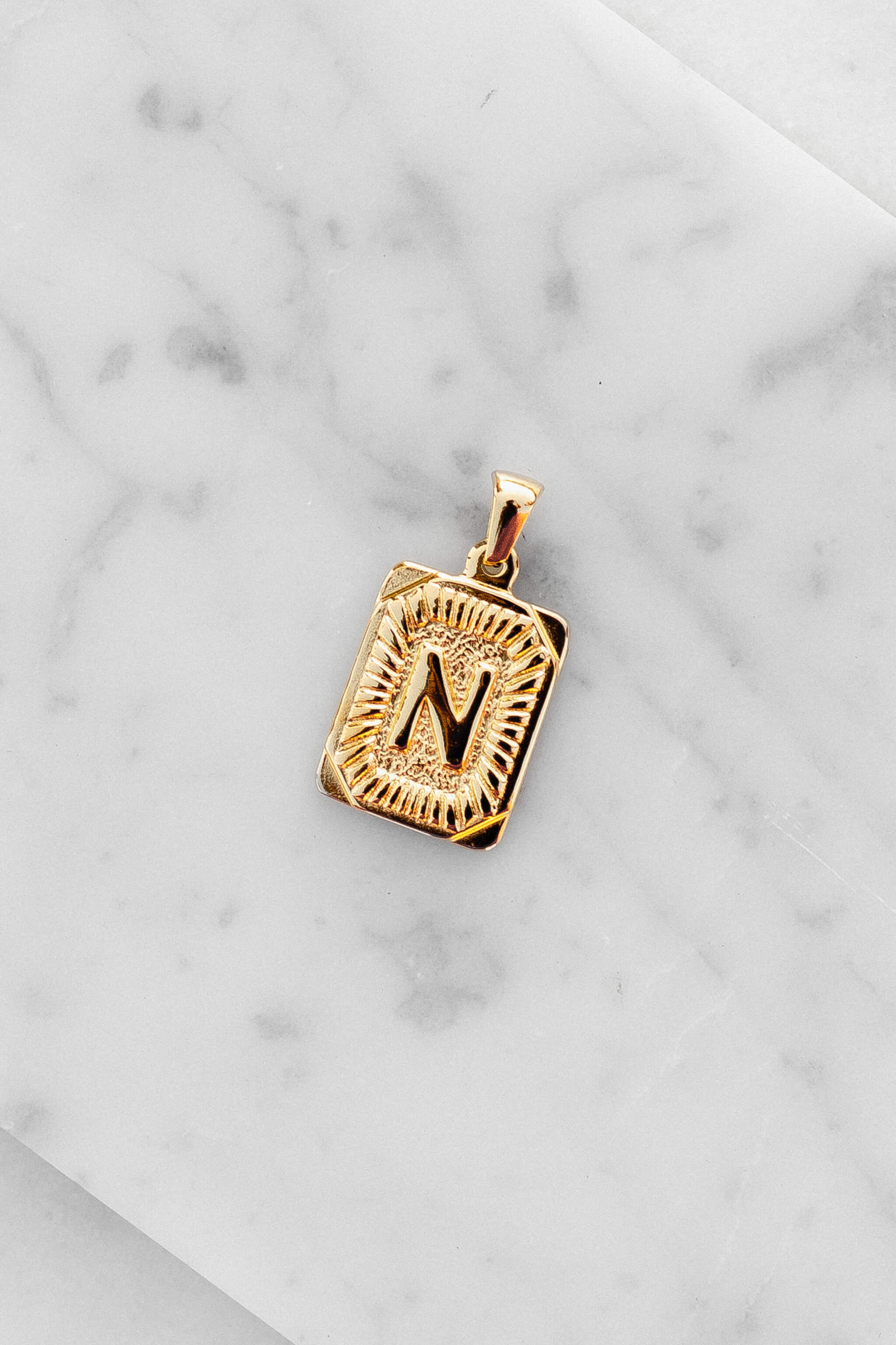 Gold Monogram Letter "N" Charm laying on a marble