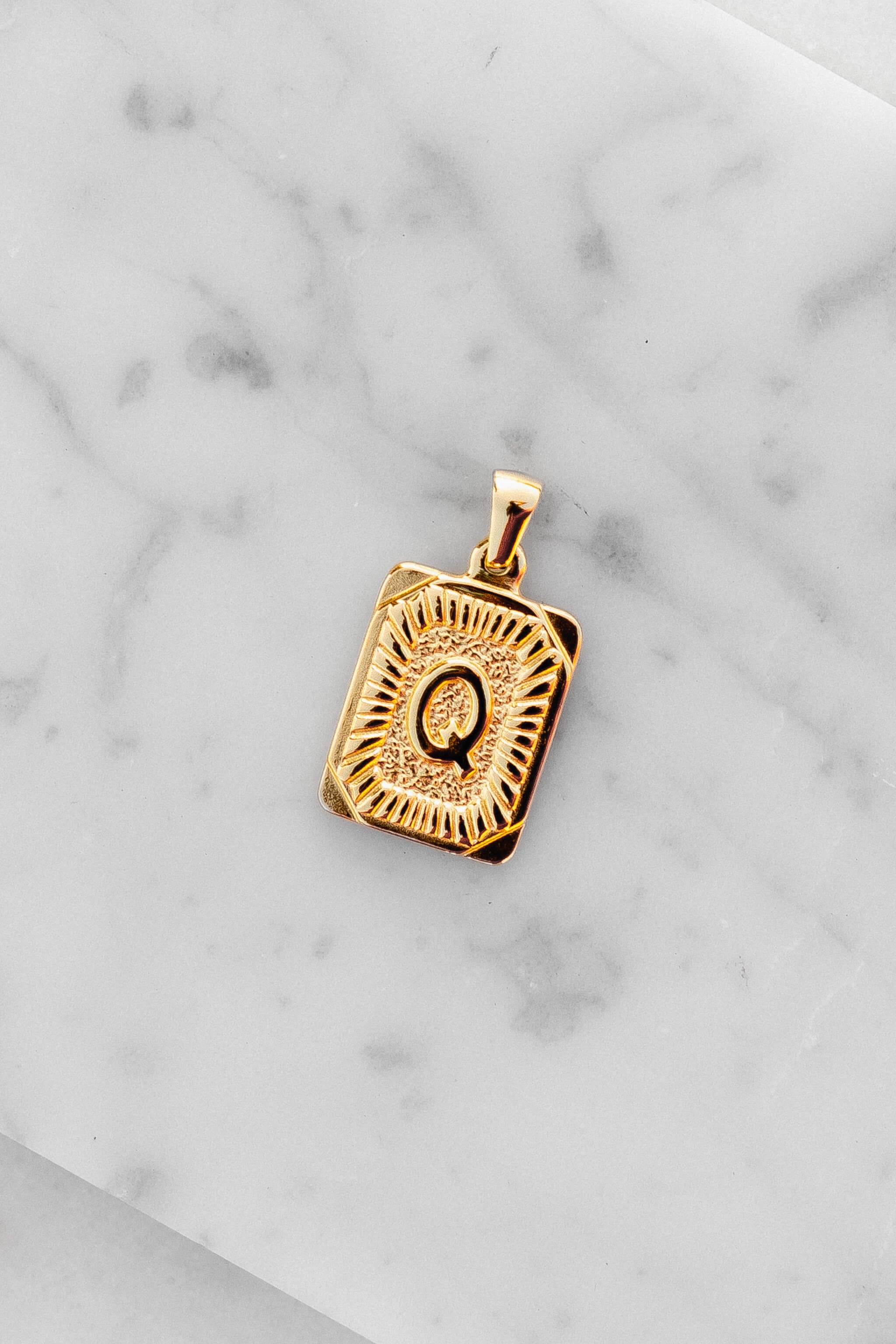 Gold Monogram Letter "Q" Charm laying on a marble