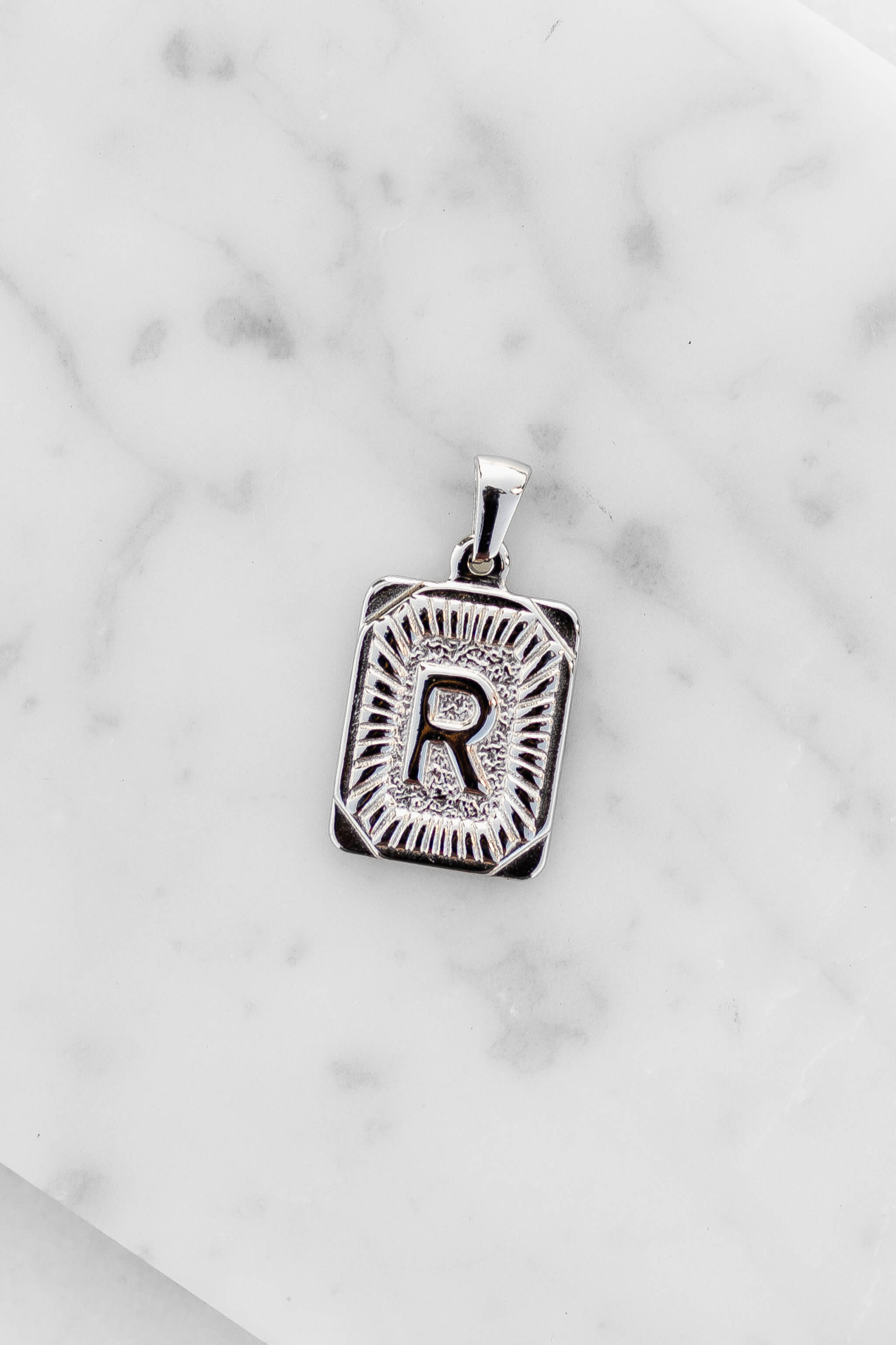 Silver Monogram Letter "R" Charm laying on a marble