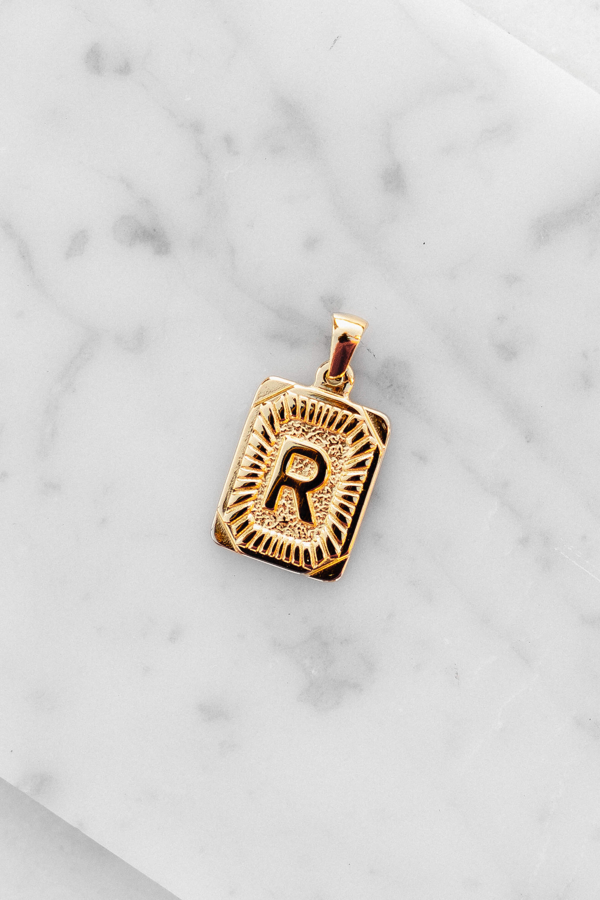 Gold Monogram Letter "R" Charm laying on a marble