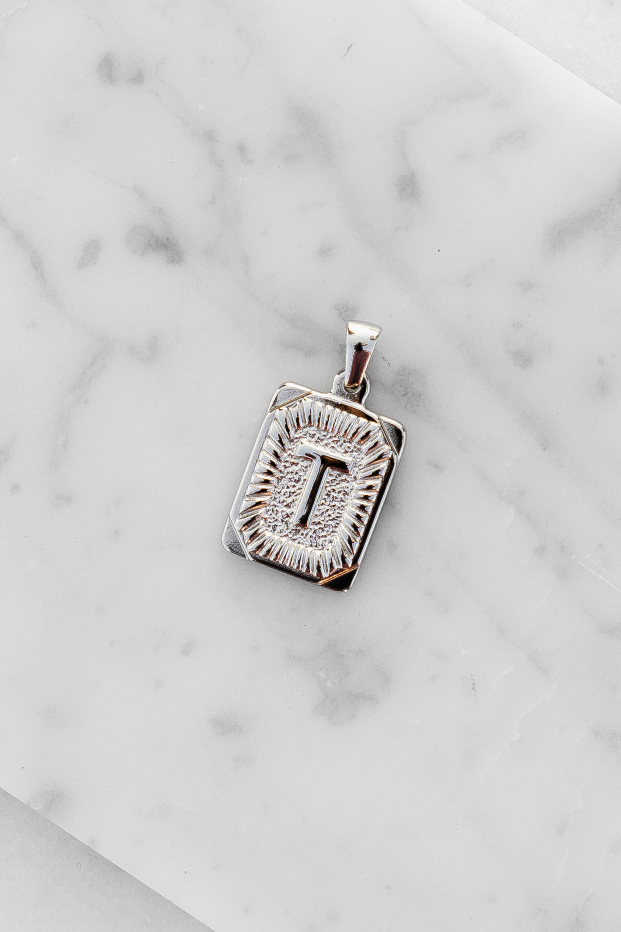 Silver Monogram Letter "T" Charm laying on a marble