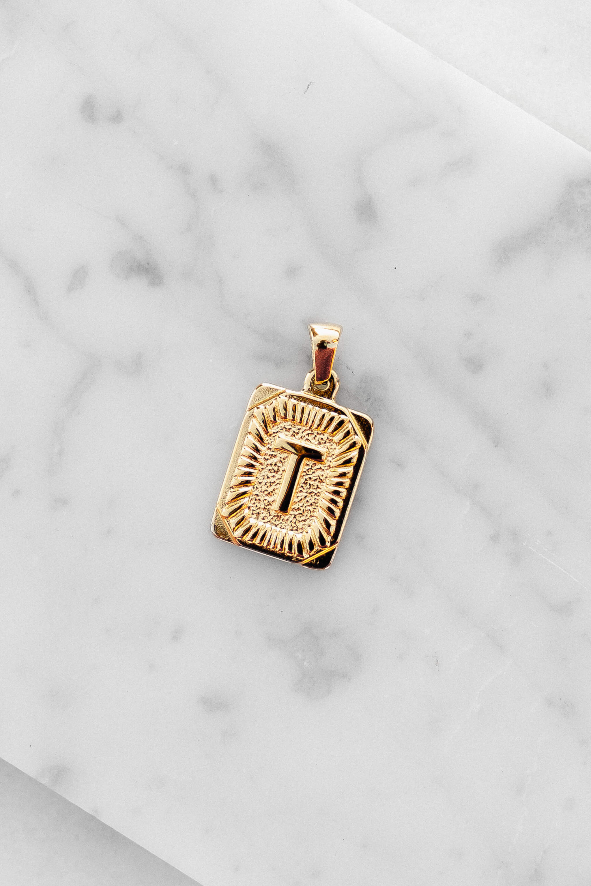 Gold Monogram Letter "T" Charm laying on a marble