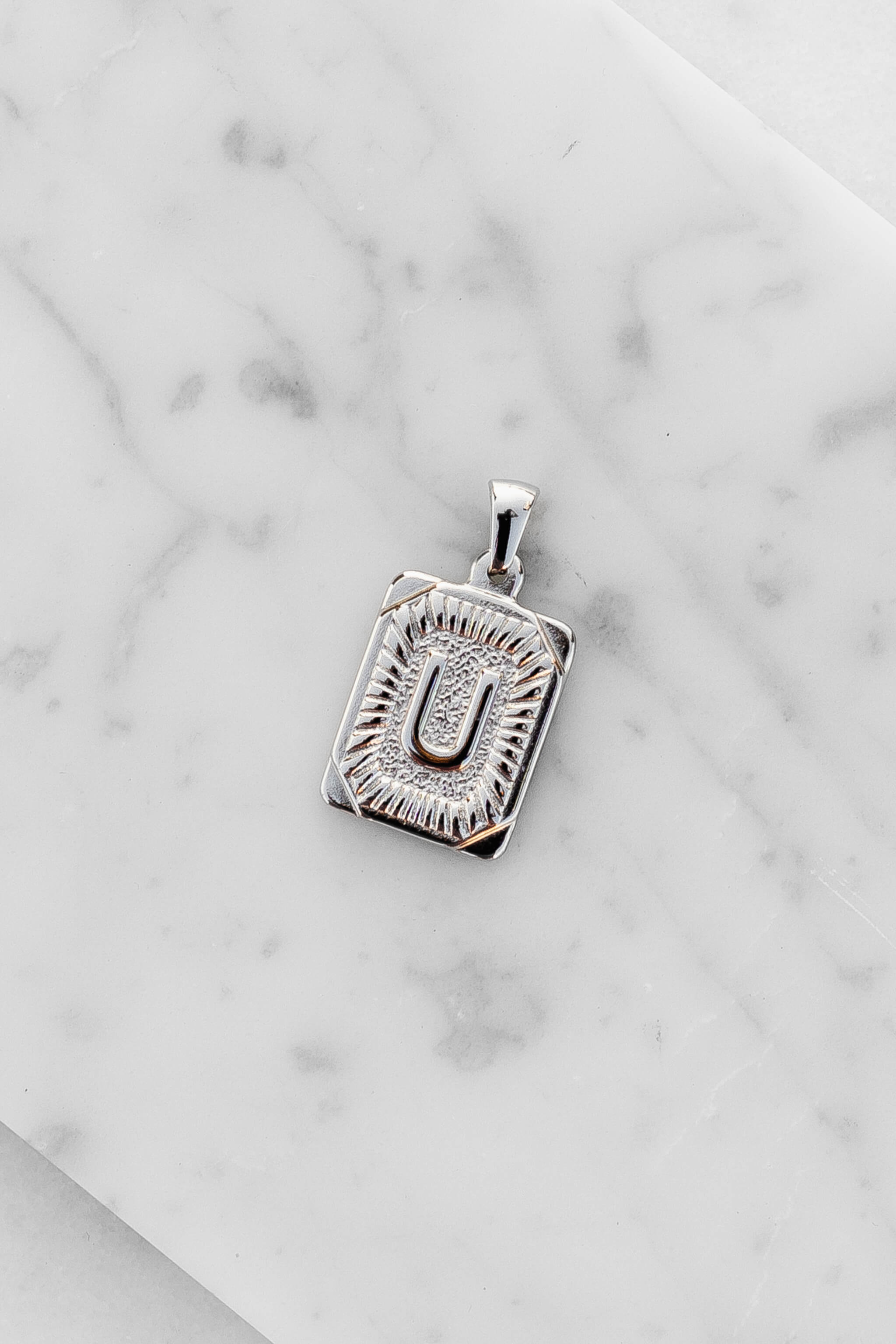Silver Monogram Letter "U" Charm laying on a marble