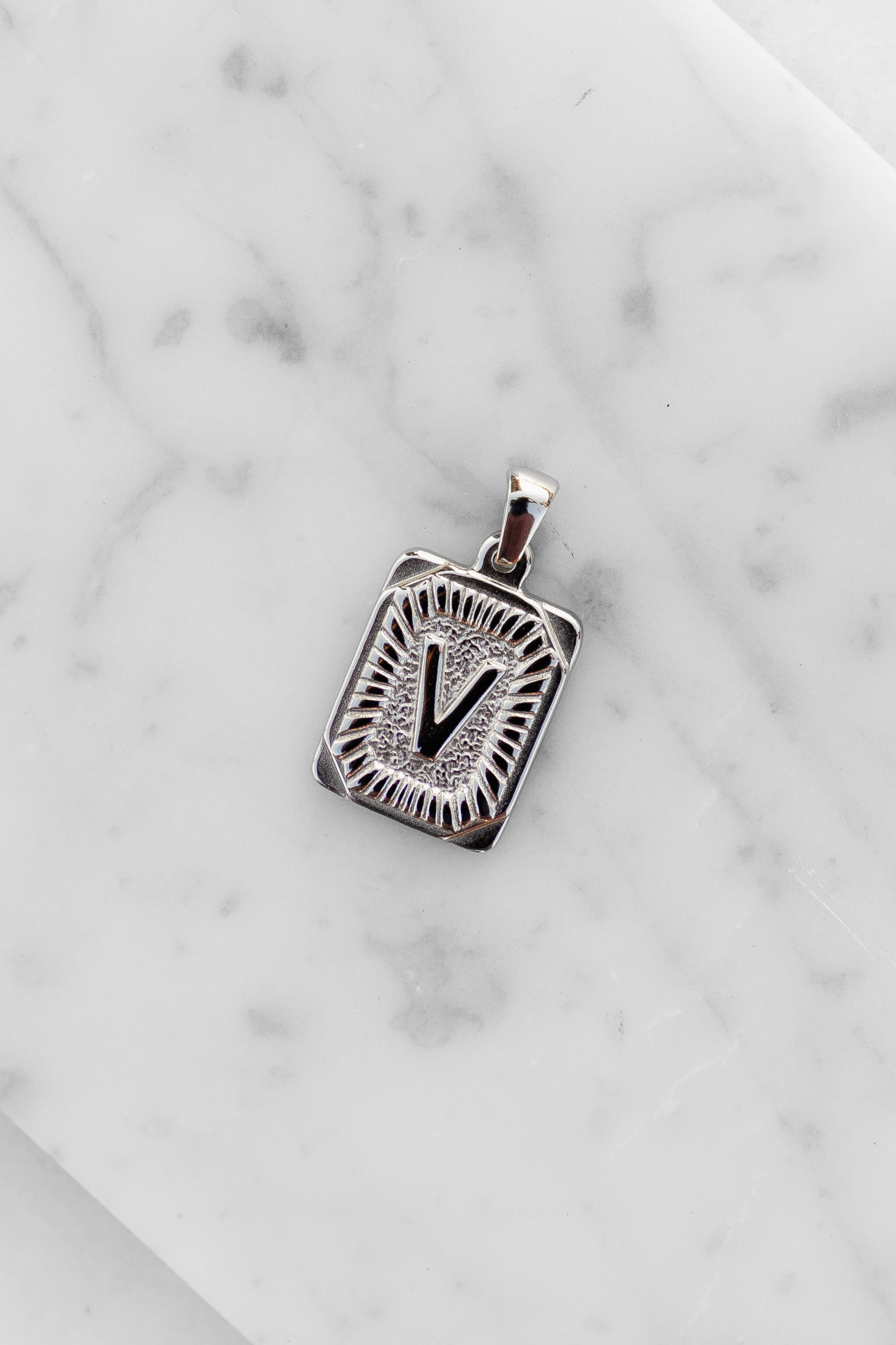 Silver Monogram Letter "V" Charm laying on a marble
