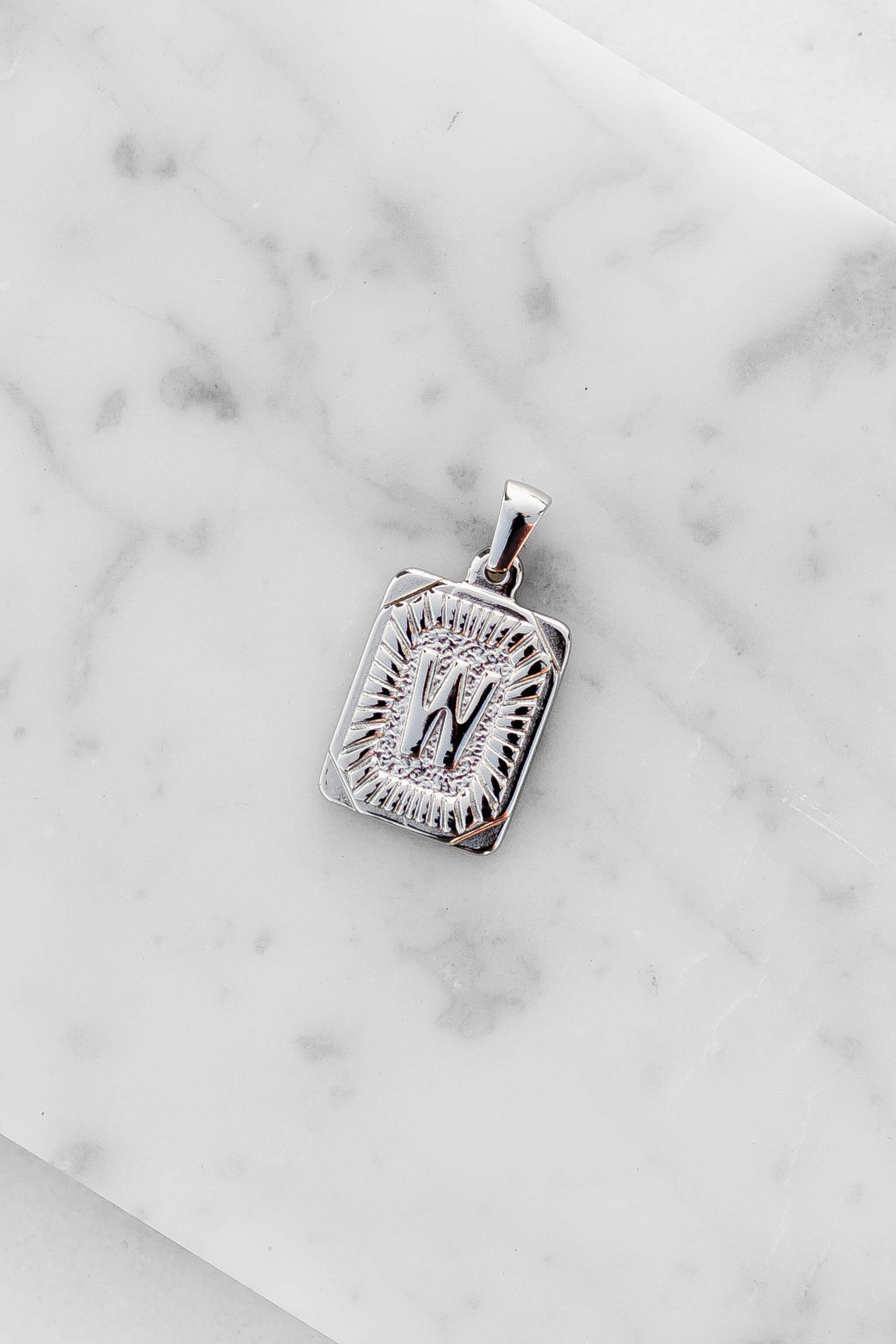 Silver Monogram Letter "W" Charm laying on a marble