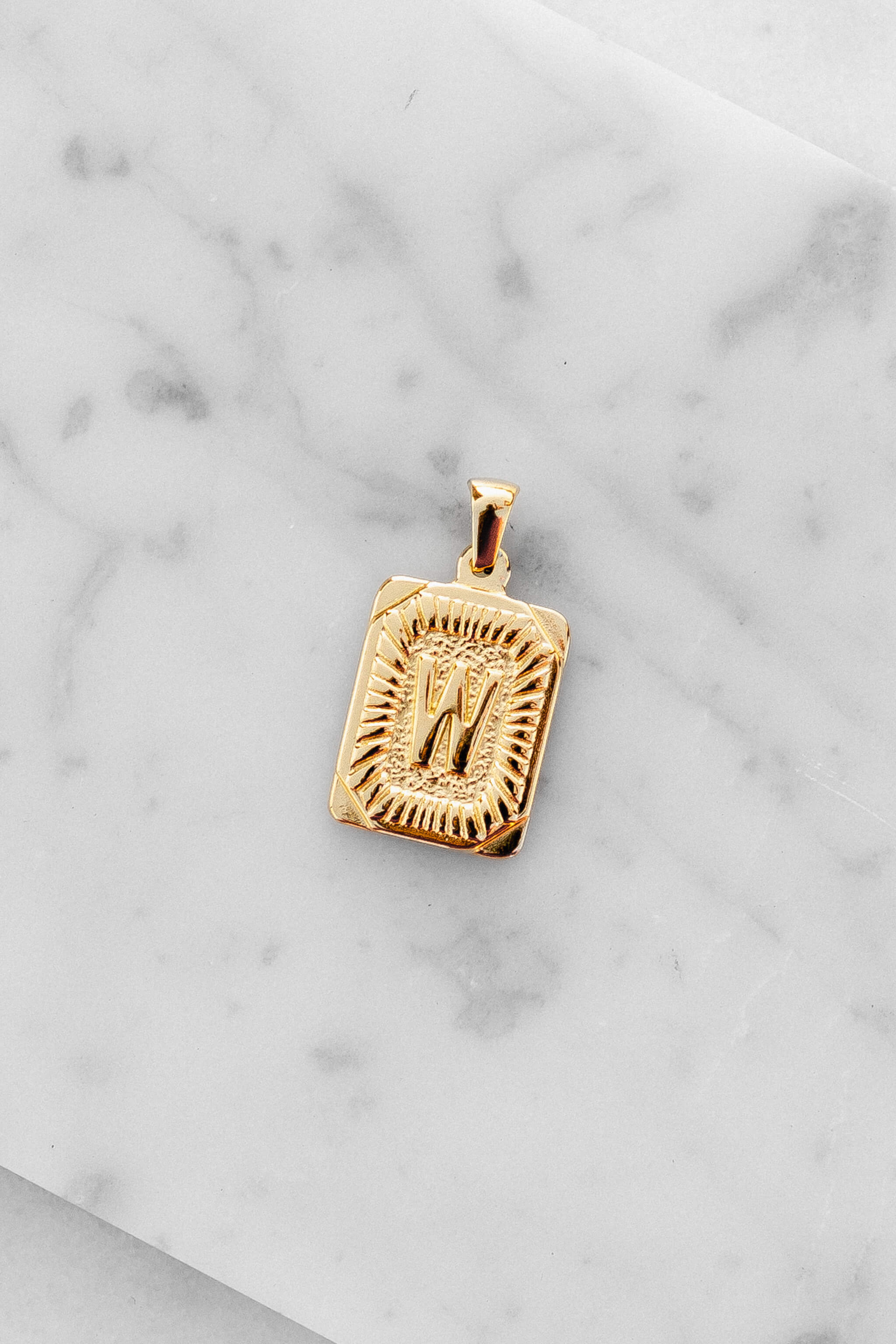 Gold Monogram Letter "W" Charm laying on a marble